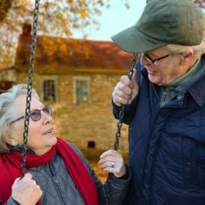 A happy elderly couple sharing a joyful moment on a swing in autumn setting.